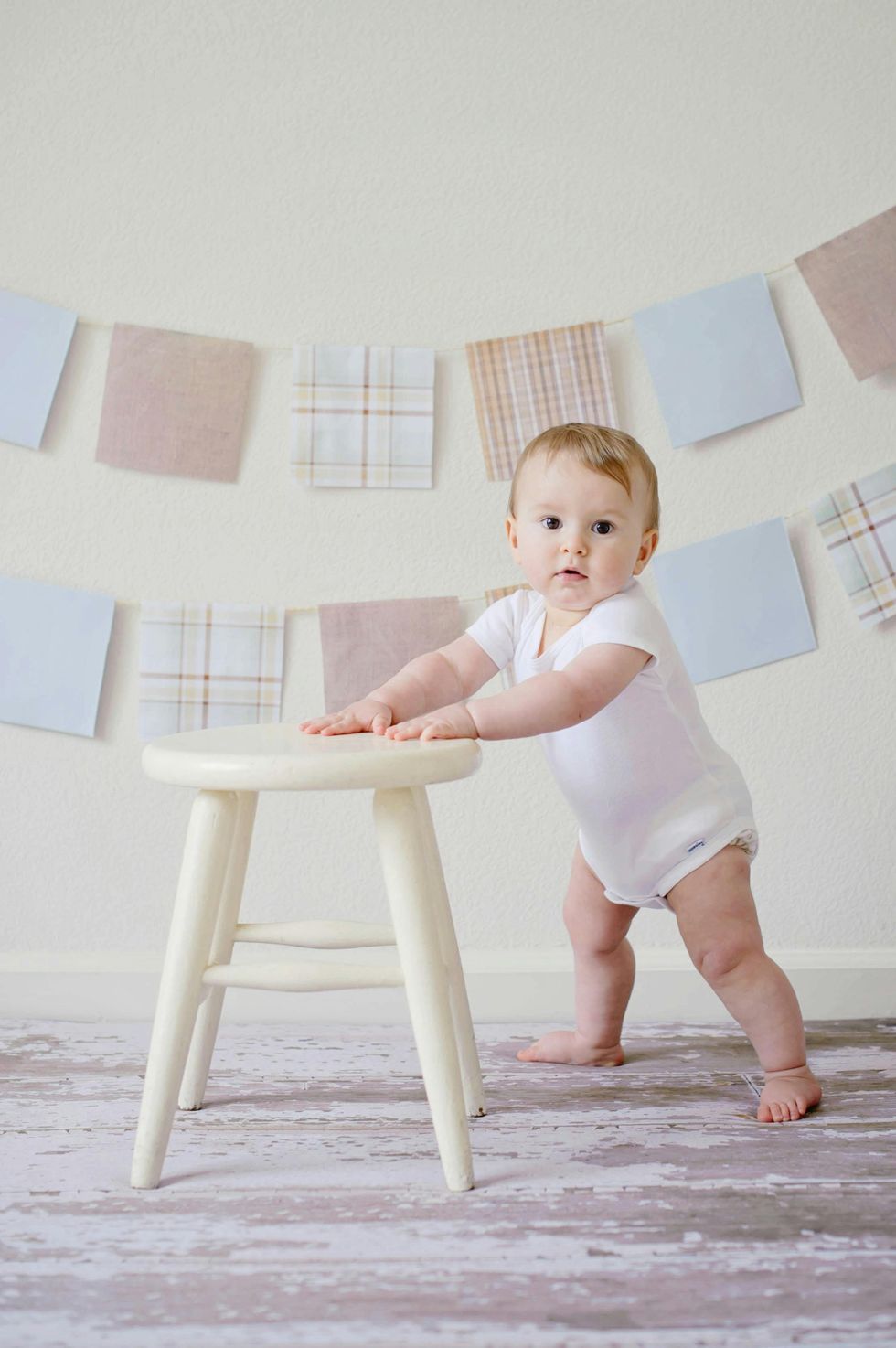 baby standing and steading themself with a white wooden stool