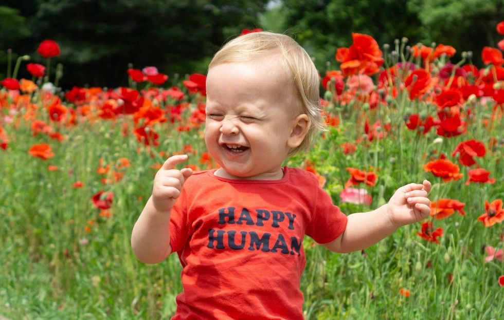 baby standing in front of red flowers