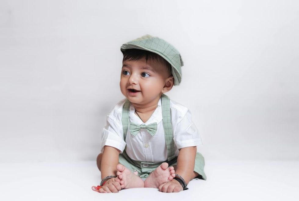 baby wearing a green hat, bowtie, and suspenders