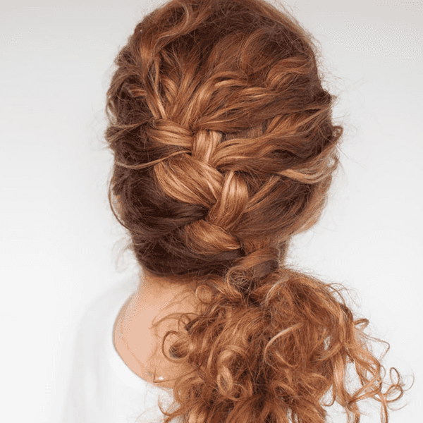 Back view of a woman with a red curly hairstyle braided into a ponytail.