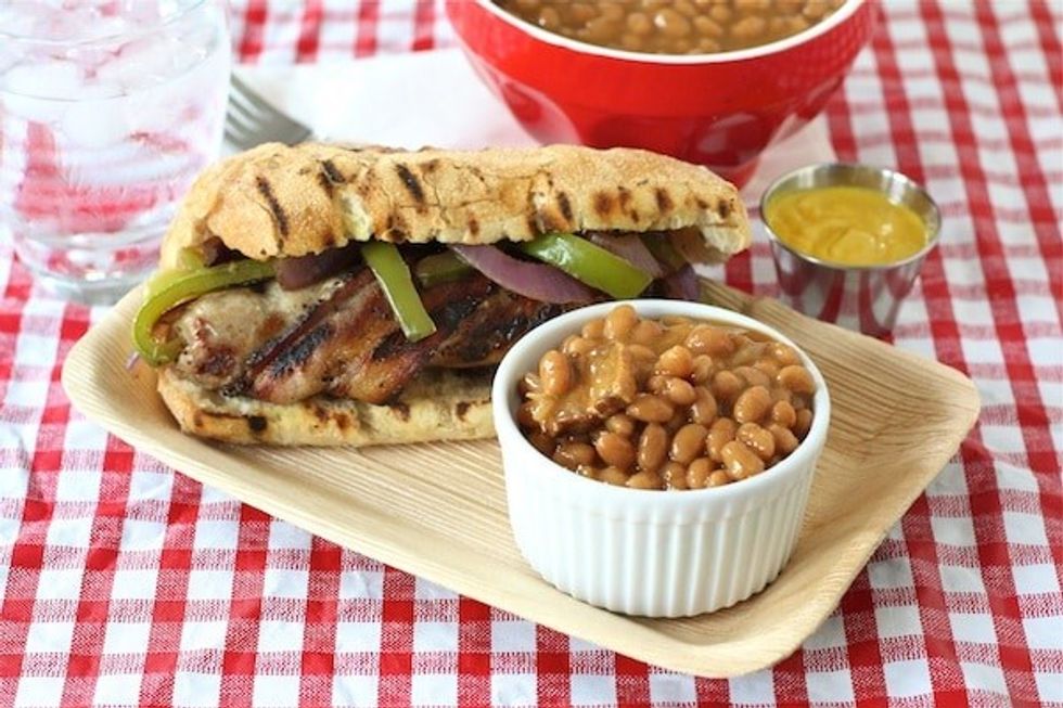 Bacon-wrapped bratwursts are on a red and white table cloth.