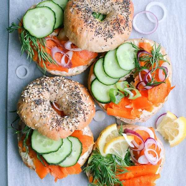Bagels with smoked salmon, cucumber, red onion, lemon, and dill on parchment paper.