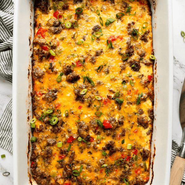 Baked casserole with cheese, sausage, red peppers, and green onions in a white dish.
