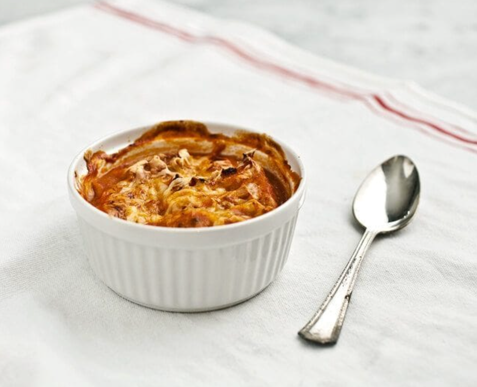 Baked dish in a white ramekin with a spoon on a white cloth.