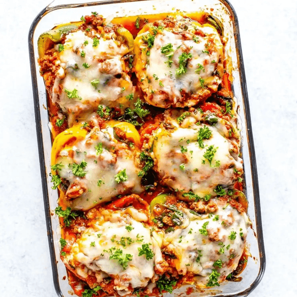 Baked stuffed bell peppers topped with melted cheese and parsley in a glass dish.