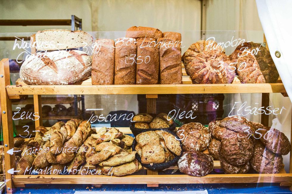 Bakery display with various breads, labeled with names and prices on a glass panel.
