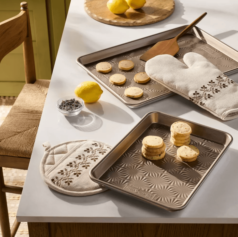 Baking sheets with cookies, oven mitt, pot holder, lemons, and spice on a kitchen counter.