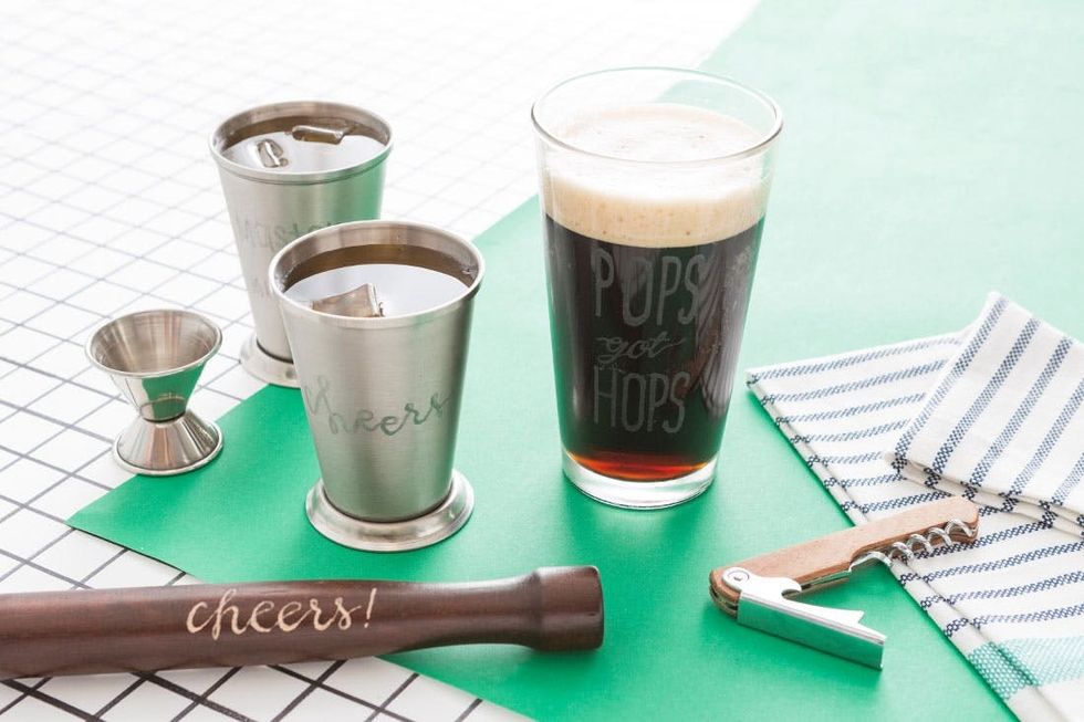Bar tools, tumbler, and pint glass on green and checkered surfaces.