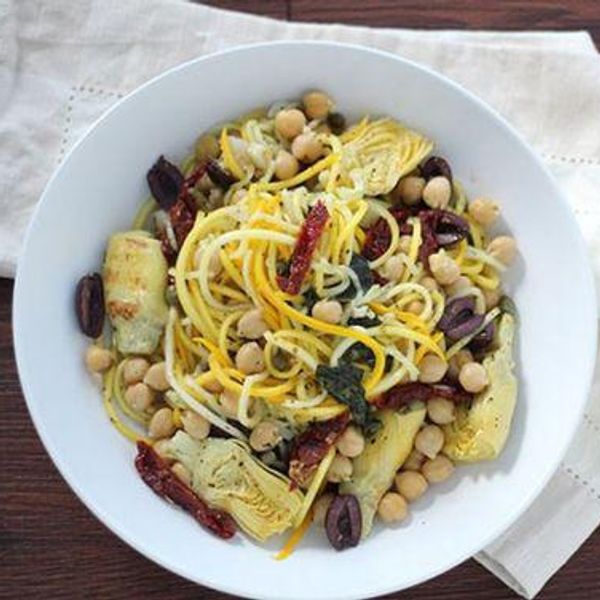 basil lemon mediterranean squash pasta in a white bowl with artichoke, chickpeas, olives, and sun dried tomatoes
