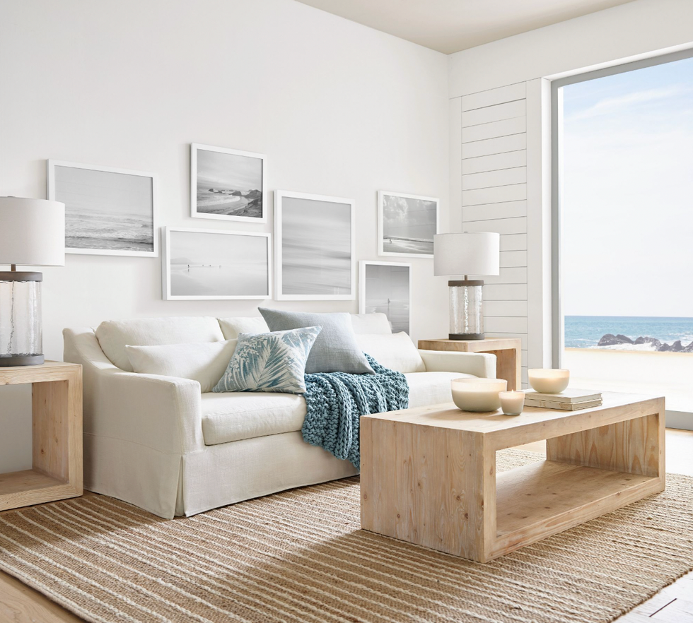 Beach-themed living room with white sofa, wood tables, ocean view, and wall art.