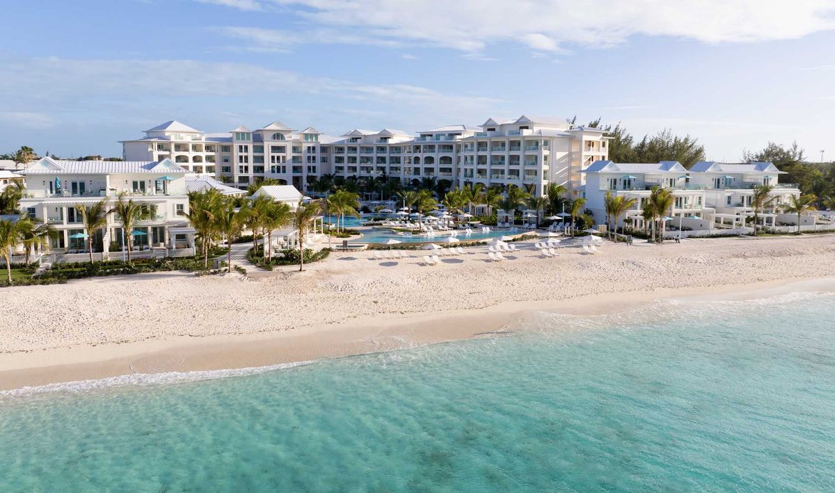 Beachfront resort with white sand, turquoise water, and palm trees under a clear blue sky.