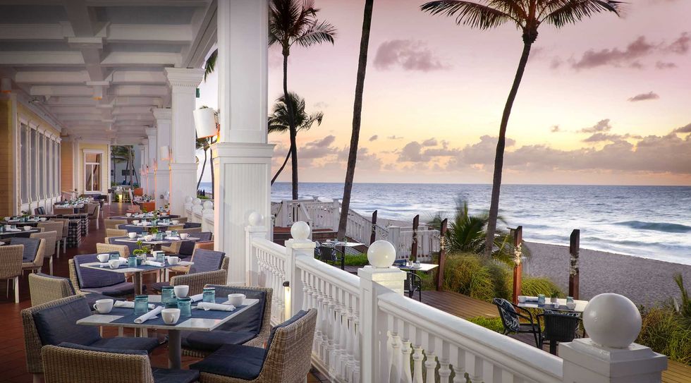 Beachfront restaurant terrace at sunset with set tables and ocean view.