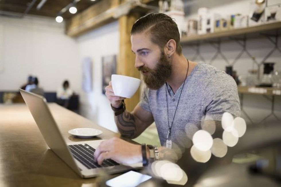 Bearded man drinking coffee at laptop in cafe