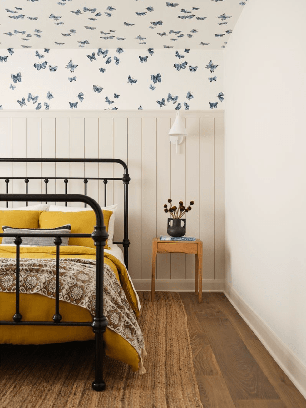 Bedroom with yellow bedding and blue butterfly wallpaper on a white paneled wall.