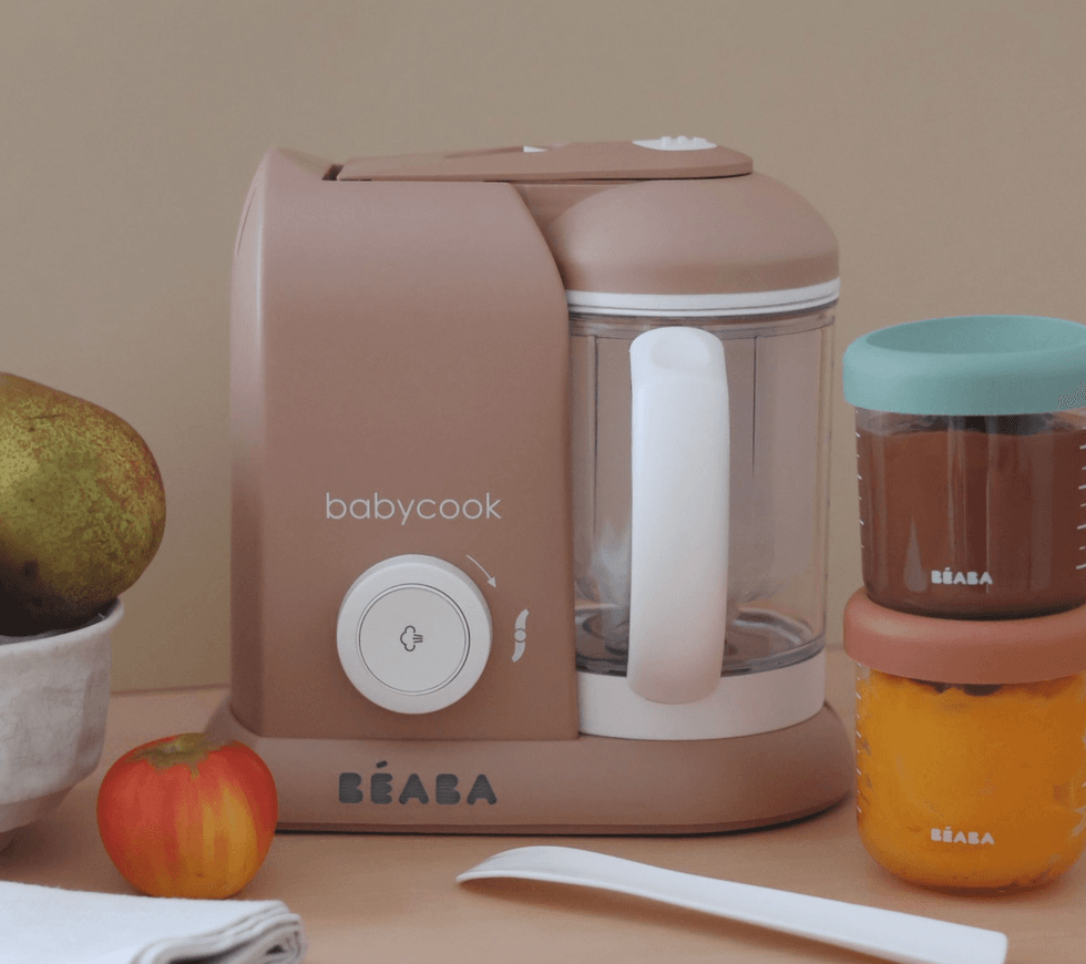 Beige baby food maker with jars and fruit nearby.