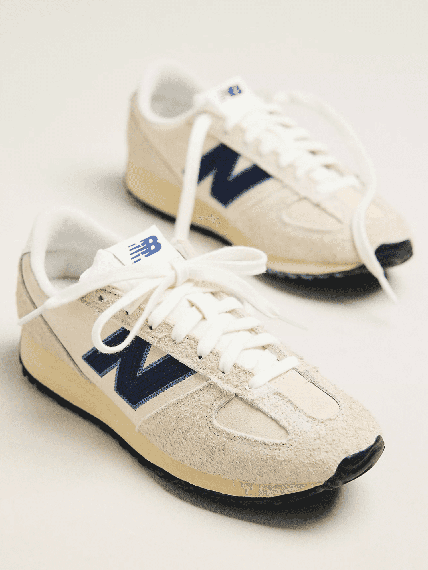 Beige sneakers with blue logo and white laces on a light background.