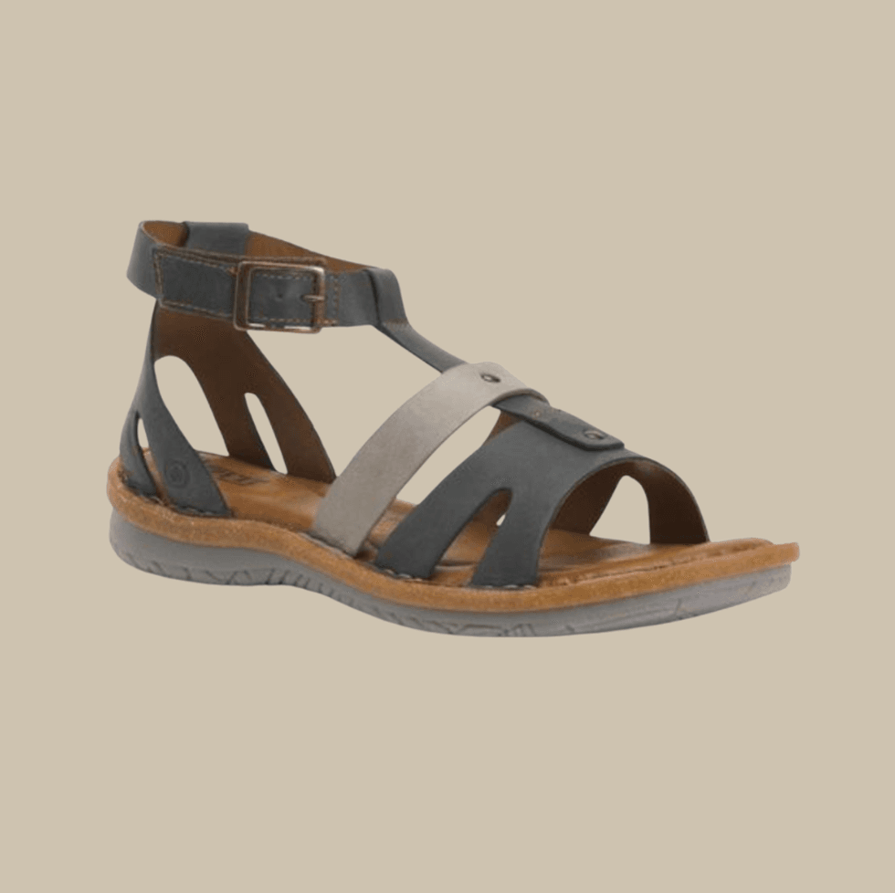Black and gray strappy sandal with buckle on a tan background.