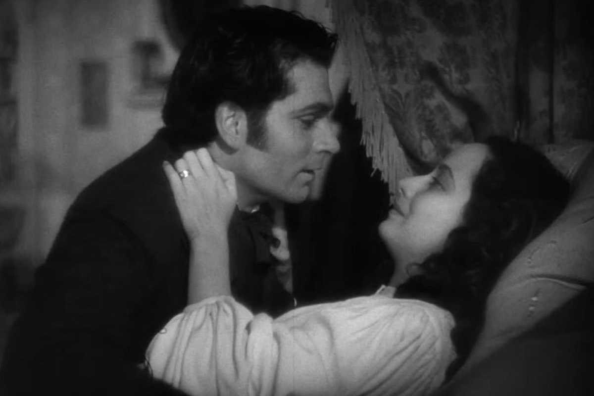 Black and white scene of a couple gazing intimately in a vintage setting.