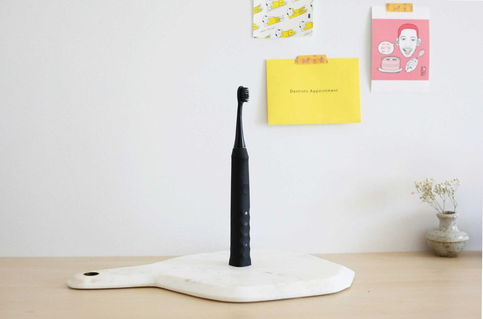 Black electric toothbrush on marble board, with notes on wall and a small vase beside it.