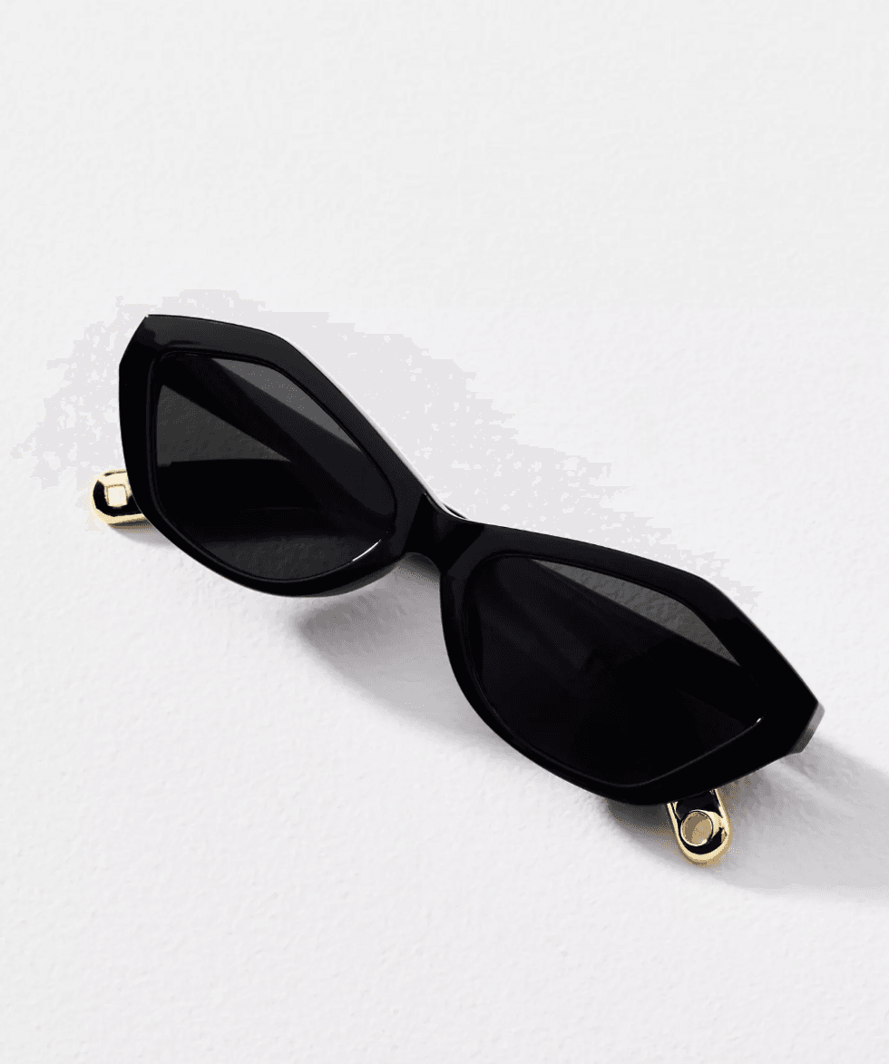 Black geometric sunglasses with gold accents on a white surface.