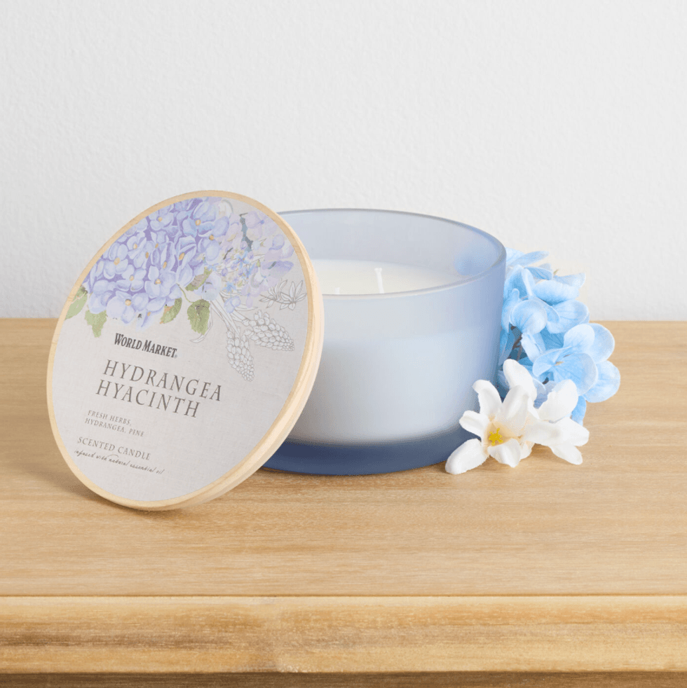 Blue candle with hydrangea lid and flowers on a wooden surface.