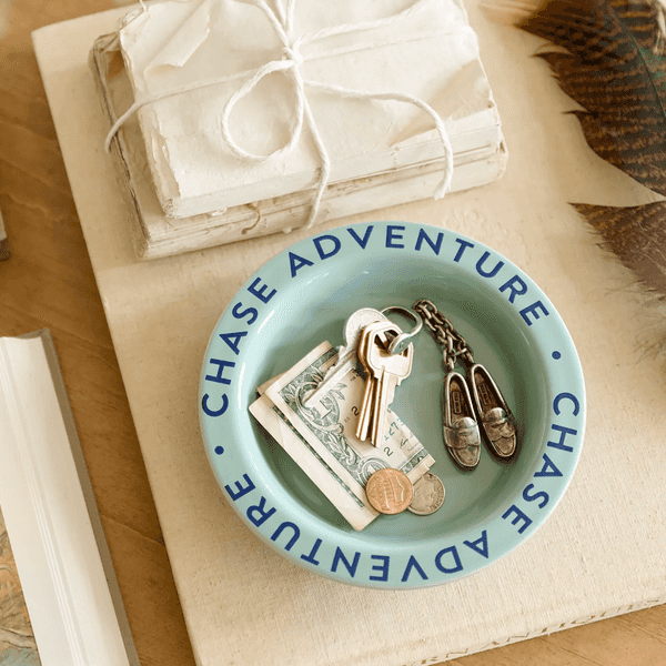 Blue dish with keys and coins, "CHASE ADVENTURE," next to books and a feather.