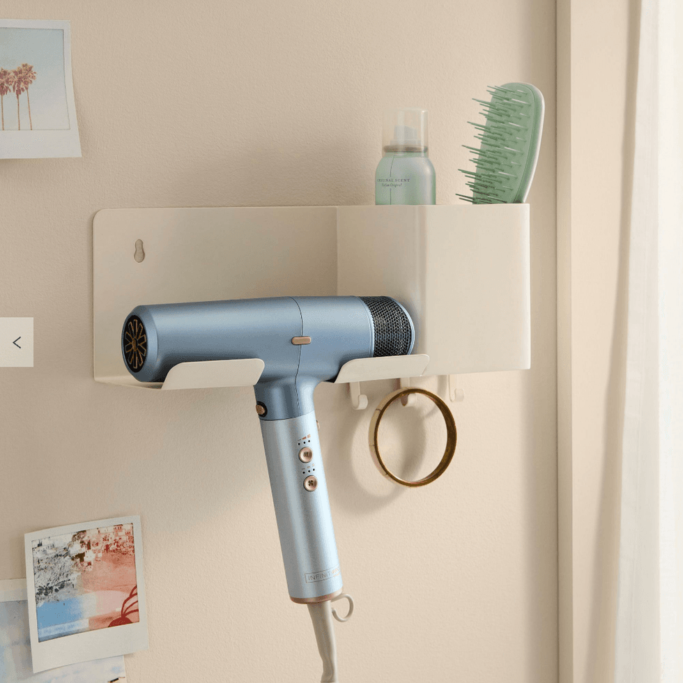 Blue hairdryer on wall shelf with brush, spray, and photos.