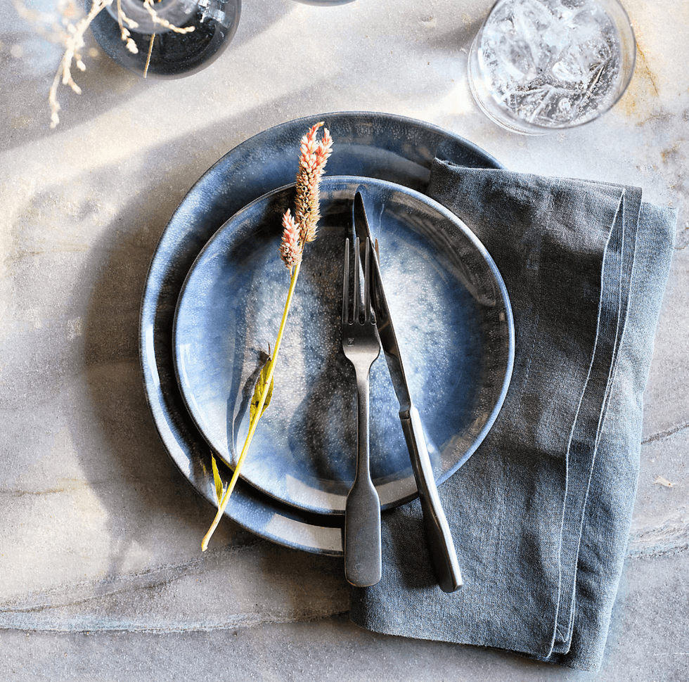 Blue plate setting with fork, knife, and floral accent on a slate table with a linen napkin.