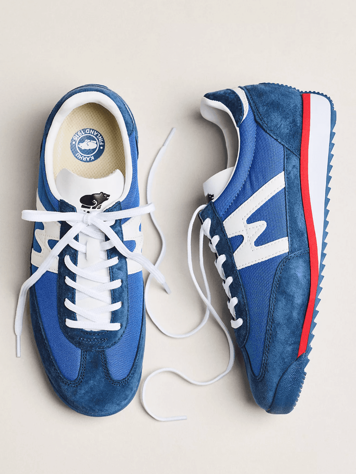 Blue sneakers with white laces and red accents on beige background.