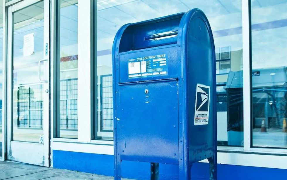 Blue USPS mailbox outside a post office building with glass doors.