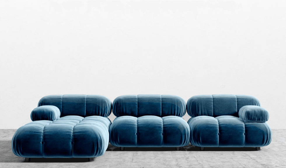 Blue velvet modular sofa with tufted cushions against a plain white wall.
