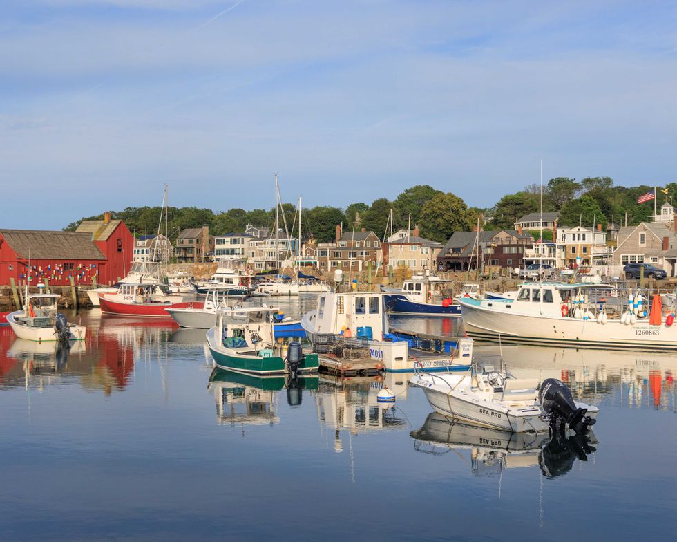 Boats in a calm harbor with a red building and coastal town in the background.