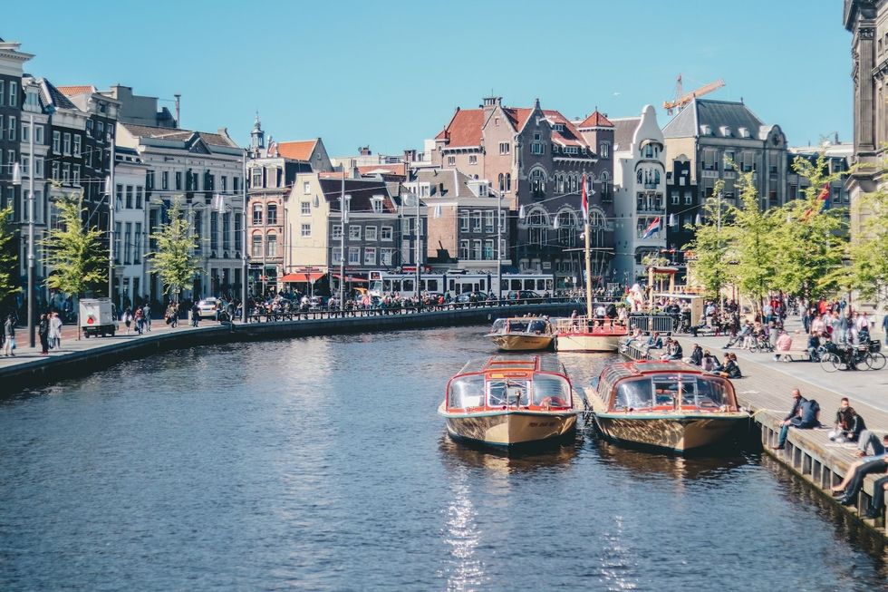 Boats on a canal with historic buildings and people strolling along the waterfront.