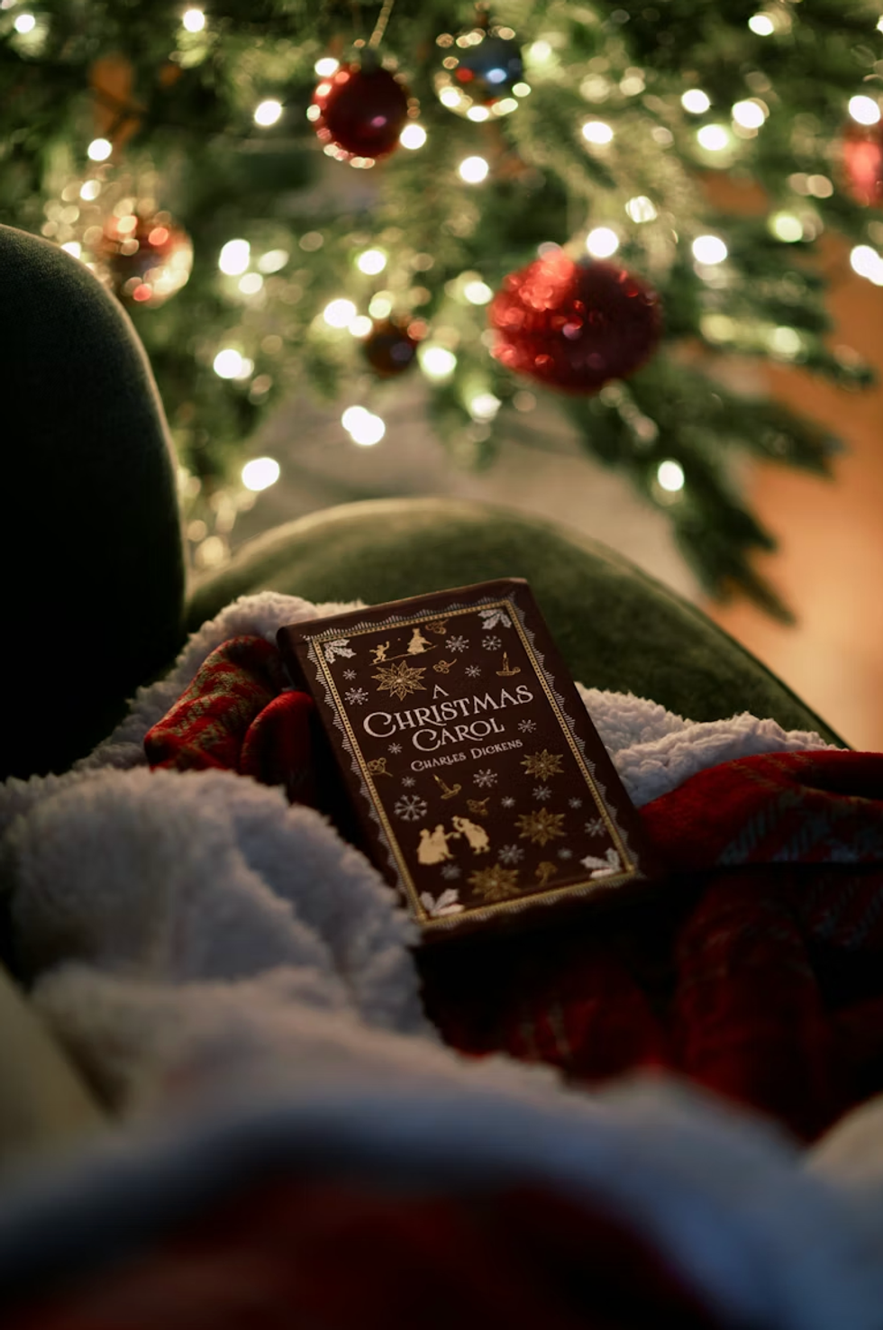 Book on chair with cozy blankets by lit Christmas tree.
