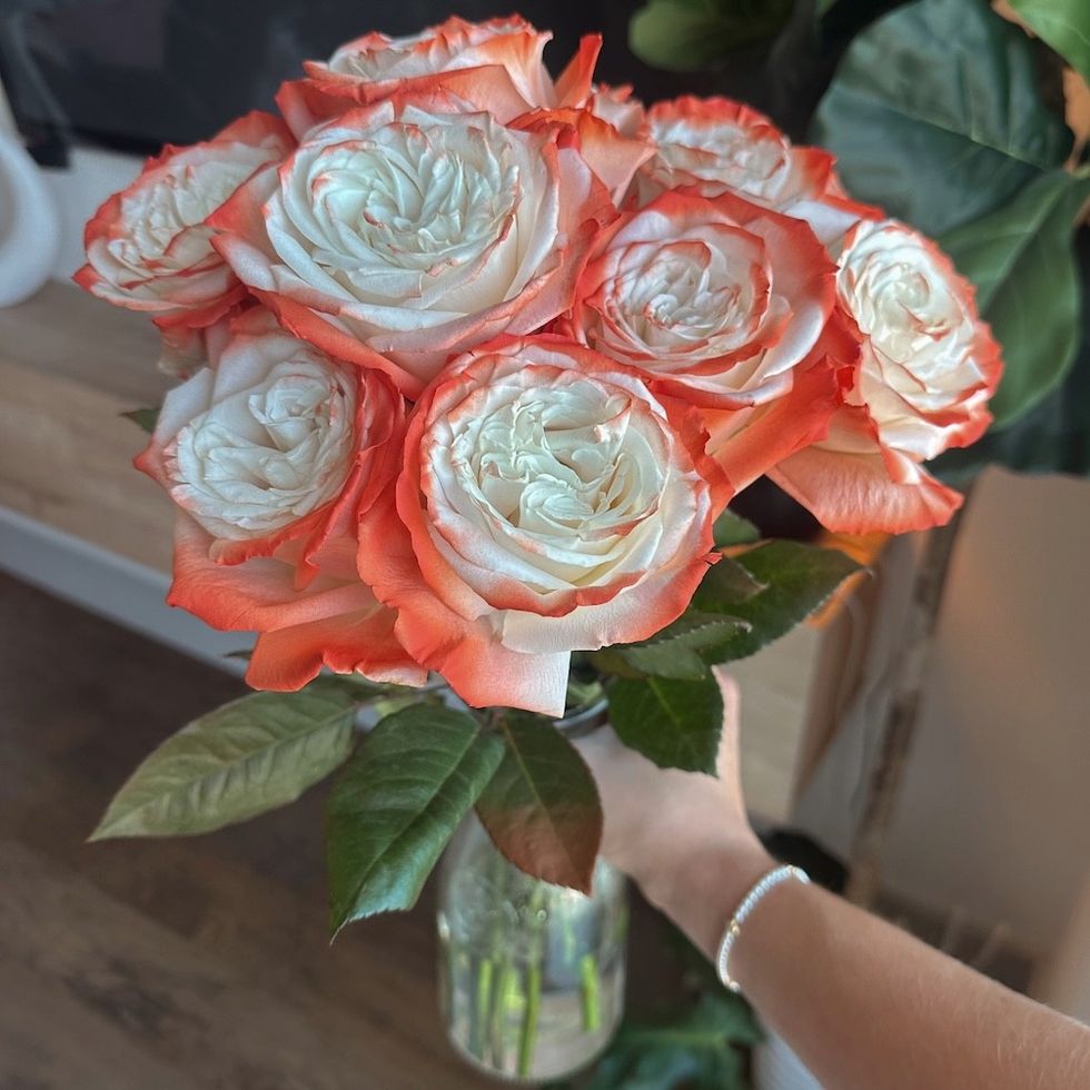 Bouquet of white roses with orange-tipped petals in a glass vase.