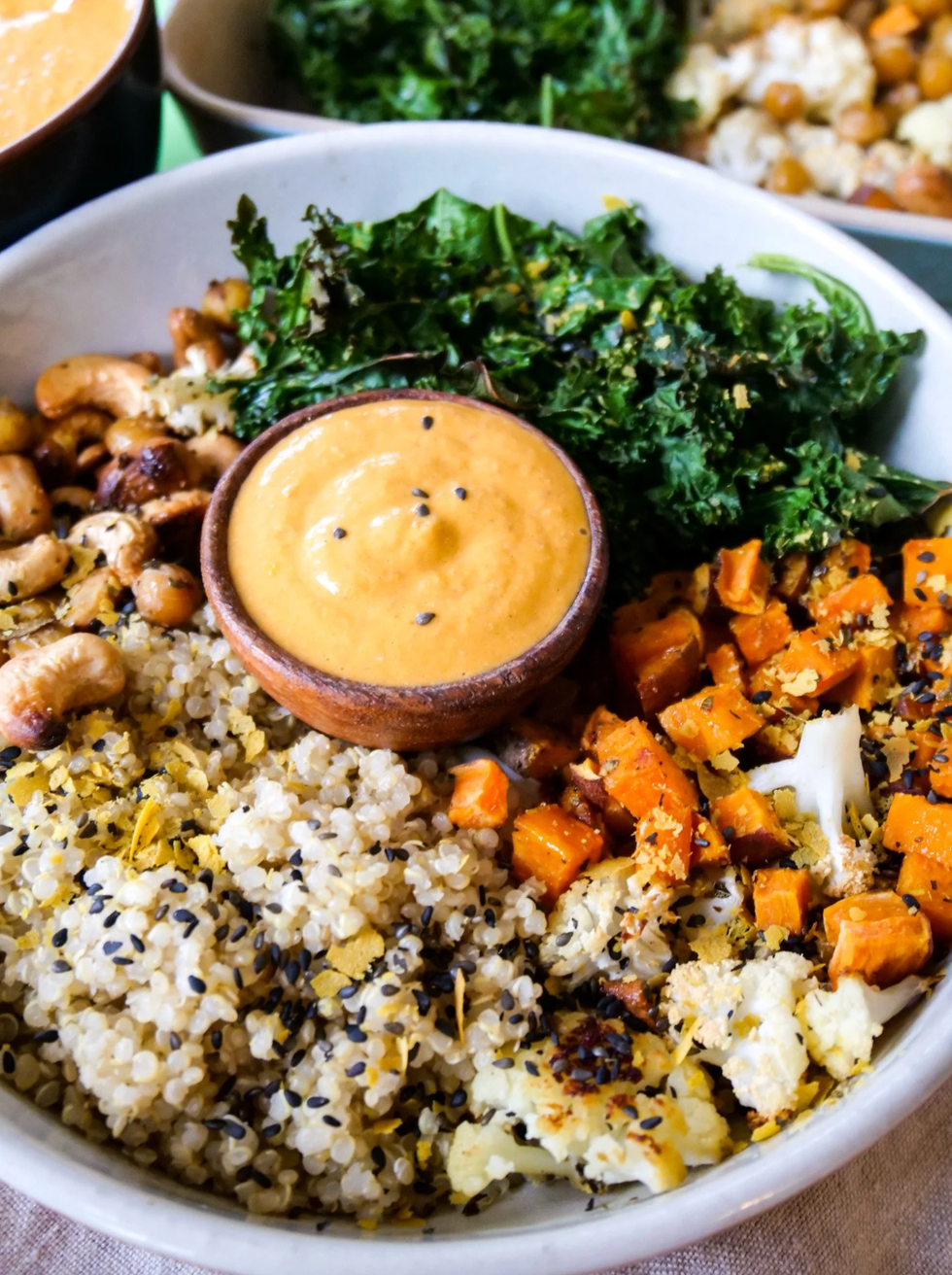 Bowl of quinoa, kale, sweet potatoes, cashews, and sauce in a wooden dish.