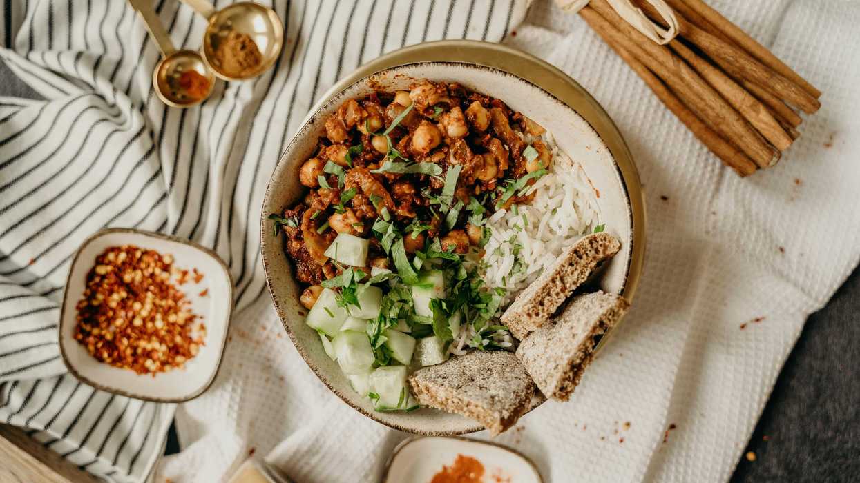 Bowl of rice, chickpeas, cucumber, herbs, and bread, with spices on a striped cloth.