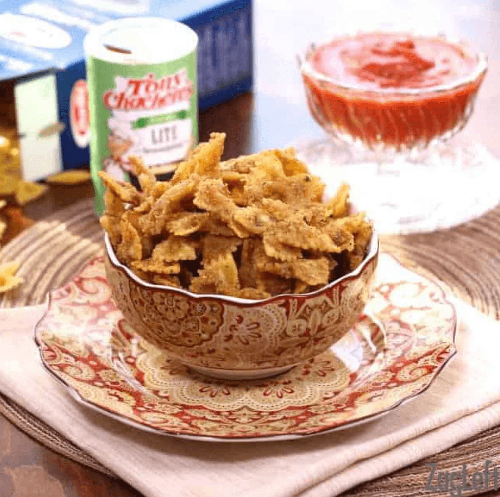 Bowl of seasoned fried bow tie pasta with dip and spice container in the background.