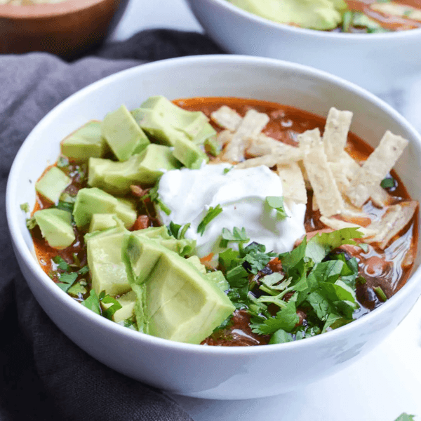 Bowl of soup with avocado, sour cream, tortilla strips, and cilantro garnish.