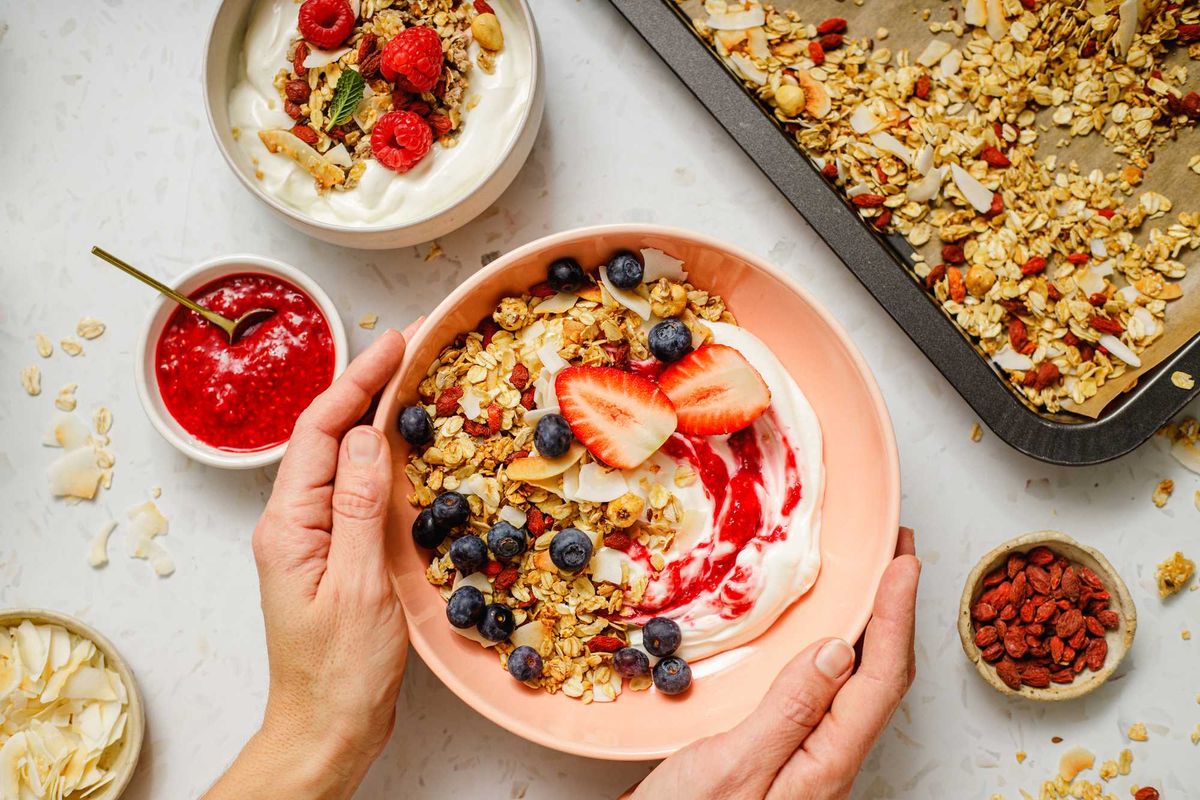 Bowl of yogurt with granola, strawberries, blueberries, and a spoonful of raspberry sauce.