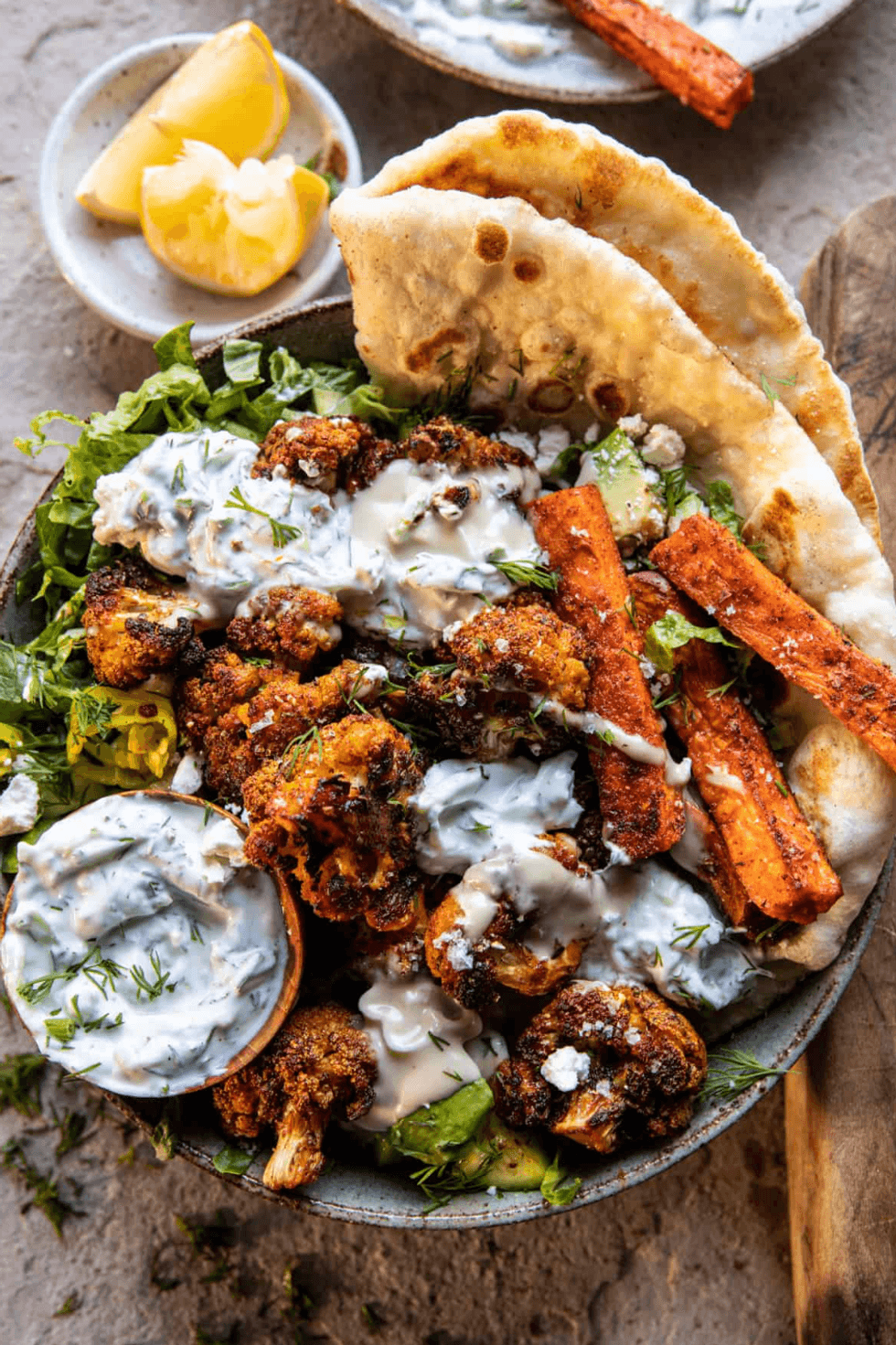 Bowl with roasted vegetables, flatbread, yogurt sauce, and lemon wedges.