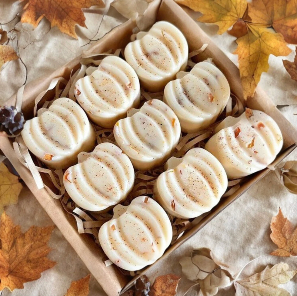 Box of pumpkin-shaped soaps on autumn leaves background.