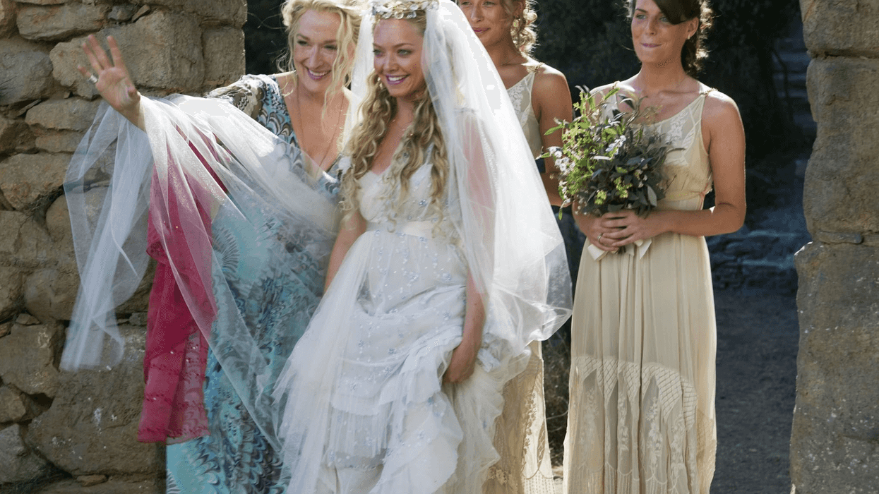 Bridal party walking through stone archway, bride in white with veil, others in light dresses.