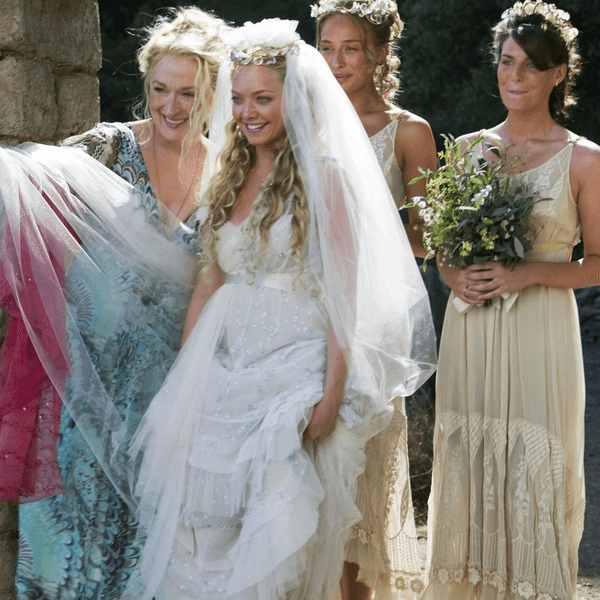 Bridal party walking through stone archway, bride in white with veil, others in light dresses.