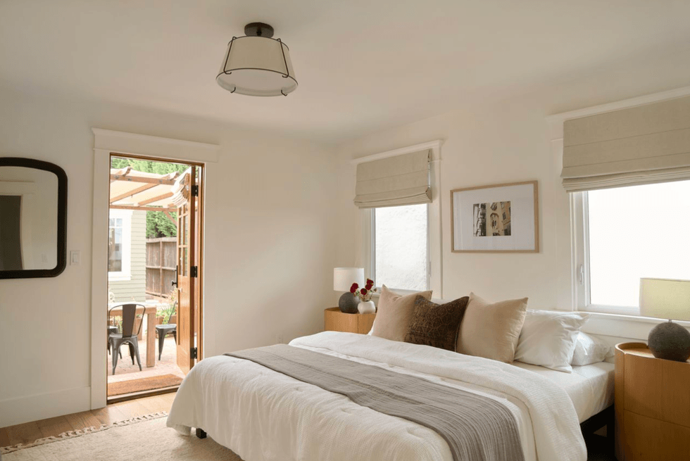 Bright bedroom with a bed, pillows, and an open door to a patio with chairs.