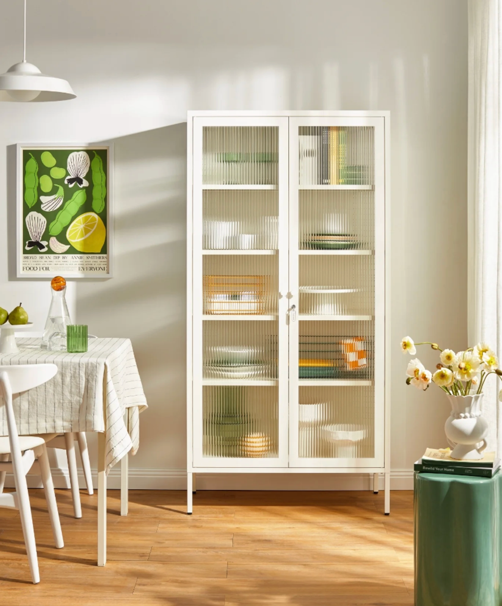 Bright dining area with white cabinet, table setting, floral decor, and green-themed wall art.