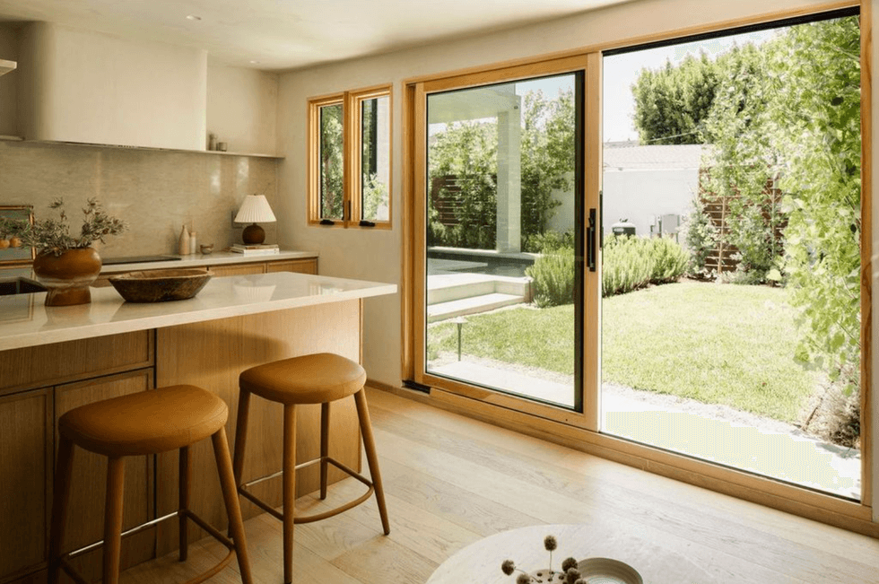Bright kitchen with bar stools and large glass doors to a lush garden.