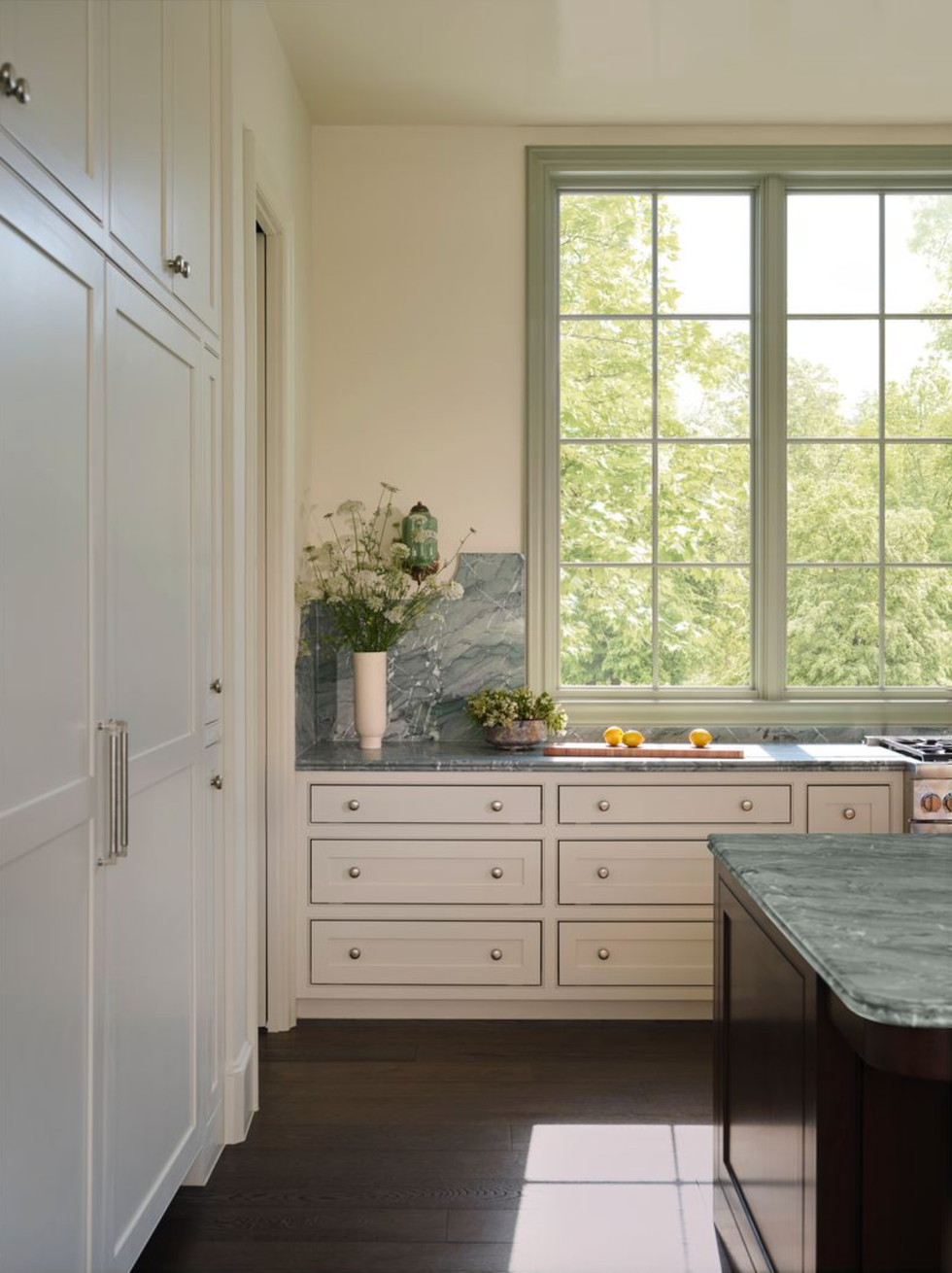 Bright kitchen with large window, white cabinets, and decorative greenery.