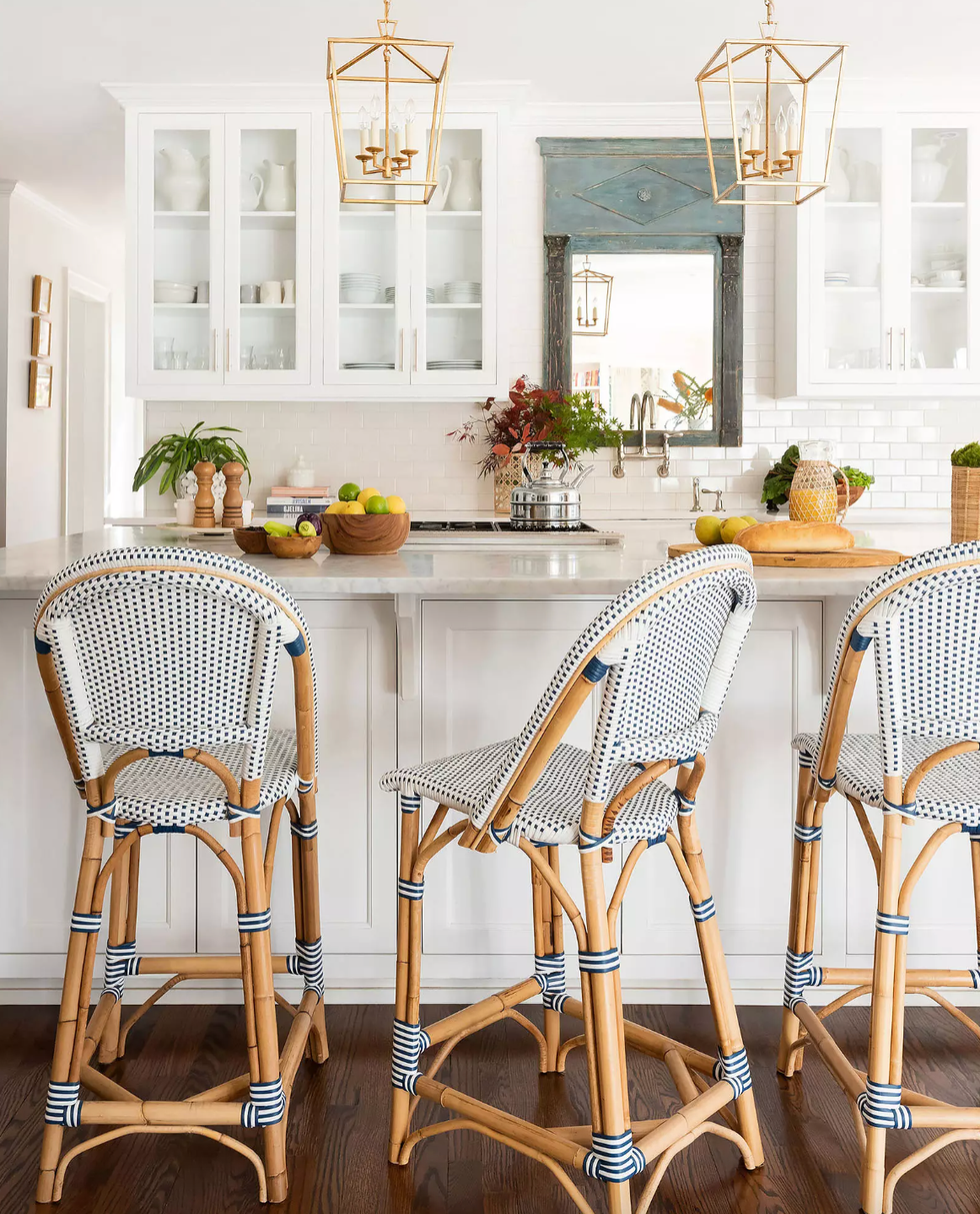 Bright kitchen with wicker barstools, white cabinets, and decorative plants.