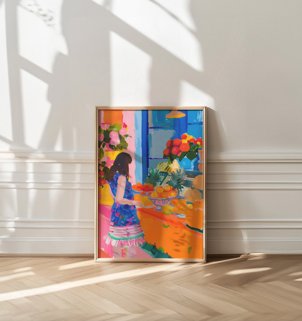 Bright painting of a woman in a blue dress buying fruit; framed and leaning on a sunlit wall.